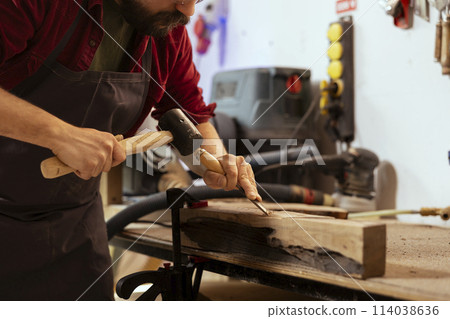 Skilled carpenter meticulously carving intricate designs into wood using chisel and hammer in assembly shop. Craftsman in woodworking workshop shaping wooden pieces with tools Skilled carpenter meticulously carving intricate designs into wood using chisel and hammer in assembly shop. Craftsman in woodworking workshop shaping wooden pieces with tools 114038636