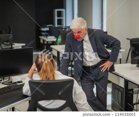 Elderly Caucasian man wearing a clown nose swears at his subordinate in the office.  114038801
