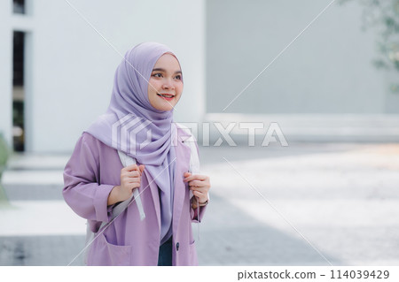 Muslim university student holding a tablet while standing outdoors on campus. Muslim university student holding a tablet while standing outdoors on campus. 114039429