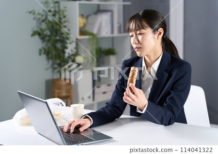 A businesswoman working while eating a late-night snack 114041322