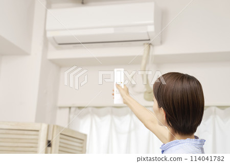 A woman using an air conditioner remote control A woman using an air conditioner remote control 114041782