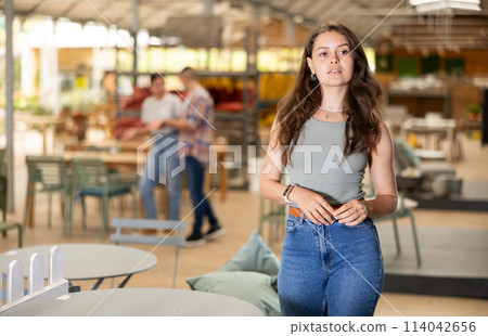 Girl buyer choose table desk in garden furniture store showroom Girl buyer choose table desk in garden furniture store showroom 114042656