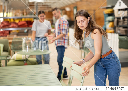 Pensive girl choosing patio chairs at garden furniture store 114042671