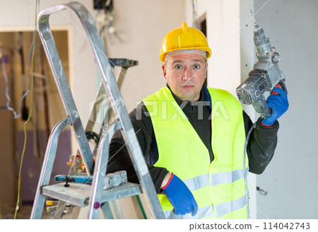 Portrait of builder handyman working with electric drill in repairable room 114042743