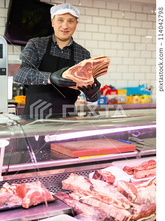 Butcher demonstrating piece of fresh raw veal chop on bone 114042798