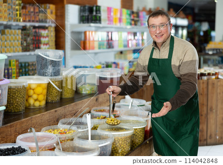 Man in supermarket, scooping marinated olives from bucket with ladle Man in supermarket, scooping marinated olives from bucket with ladle 114042848