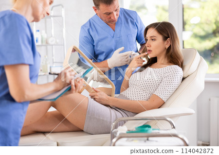 Male plastic surgeon consulting woman before facial contouring Male plastic surgeon consulting woman before facial contouring 114042872
