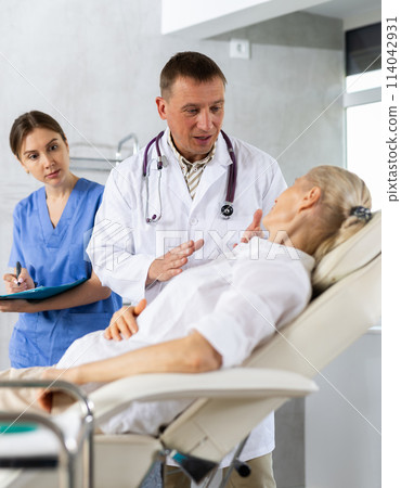 Male beautician, together with a nurse, examines the face of an mature woman and plans facelift procedures. Male beautician, together with a nurse, examines the face of an mature woman and plans facelift procedures. 114042931