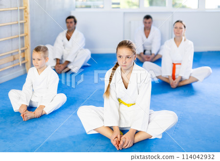 Family during group karate training with trainer in gym performs stretching of muscles by performing butterfly exercise Family during group karate training with trainer in gym performs stretching of muscles by performing butterfly exercise 114042932