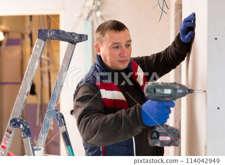 Portrait of builder handyman working with electric drill in repairable room Portrait of builder handyman working with electric drill in repairable room 114042949