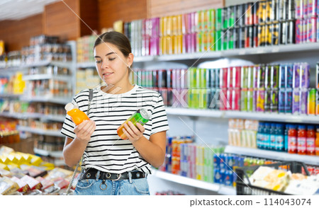 Young girl choosing colored drinks in drinks section of supermarket Young girl choosing colored drinks in drinks section of supermarket 114043074