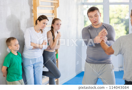 Man coach shows family students technique of performing painful modus with help of wringing hand Man coach shows family students technique of performing painful modus with help of wringing hand 114043084