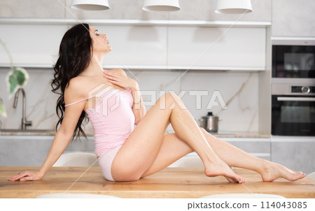 Woman in casual camisole and panties sitting on table in kitchen 114043085