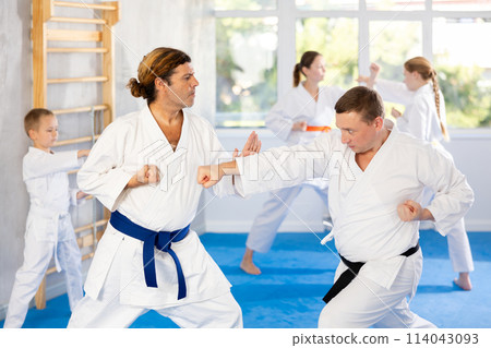 Two men at group training in gym practice karate punch block technique Two men at group training in gym practice karate punch block technique 114043093