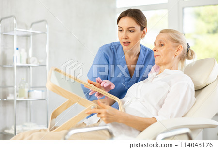 Female cosmetologist explaining facial procedure to elderly woman Female cosmetologist explaining facial procedure to elderly woman 114043176