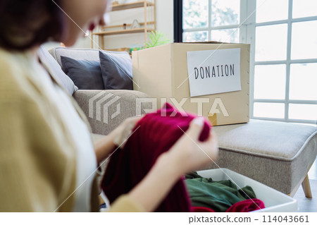 Asian young woman packing clothes at home, putting on stuff into donate box with second hand clothes Asian young woman packing clothes at home, putting on stuff into donate box with second hand clothes 114043661