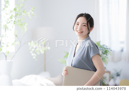 Young woman with laptop computer by the window in a beautiful office, holding a PC and smiling while looking at the camera, copy space on the left Young woman with laptop computer by the window in a beautiful office, holding a PC and smiling while looking at the camera, copy space on the left 114043978