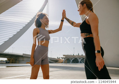 Happy female friends doing gesture of sport shake hand after exercising outside 114045944
