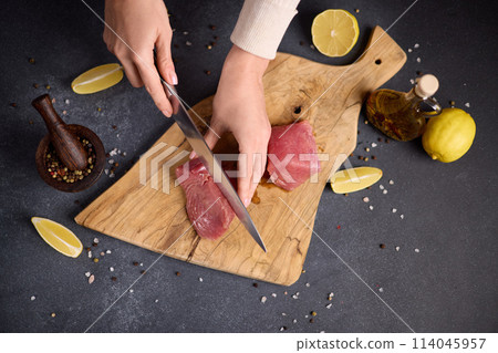Woman cut tuna steak into slices on a wooden cutting board at domestic kitchen cooking tuna carpaccio Woman cut tuna steak into slices on a wooden cutting board at domestic kitchen cooking tuna carpaccio 114045957