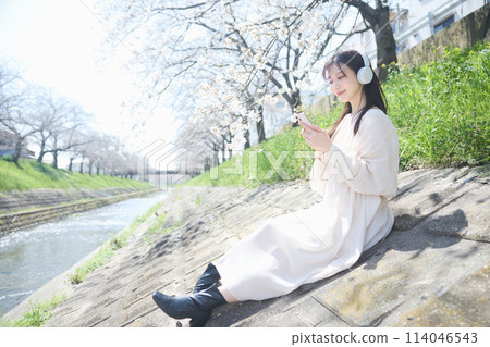 A woman listening to music under the cherry blossoms 114046543