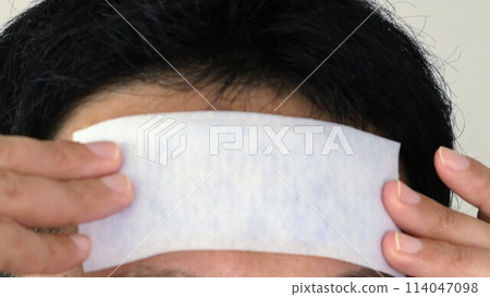 Japanese man putting a cooling sheet on his forehead Japanese man putting a cooling sheet on his forehead 114047098