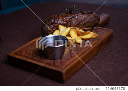 Beef steak with baked potato wedges and rosemary on a wooden board Beef steak with baked potato wedges and rosemary on a wooden board 114048678