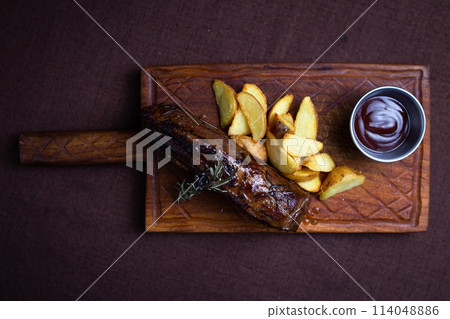 top view of the beef steak with baked potato wedges and rosemary on a wooden board 114048886