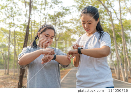 Two young female friends checking out their run time on their smart watch after their morning run at a local running park 114050716