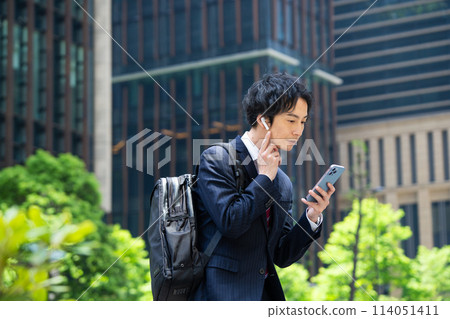 A businessman using a smartphone with wireless earphones A businessman using a smartphone with wireless earphones 114051411