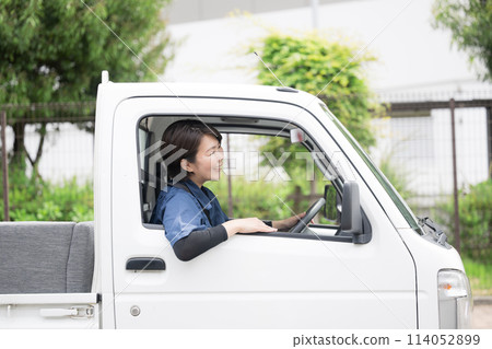 Profile of a middle-aged woman in work clothes driving a truck amidst fresh greenery. Image of transportation and delivery industry. Waste collection. Profile of a middle-aged woman in work clothes driving a truck amidst fresh greenery. Image of transportation and delivery industry. Waste collection. 114052899