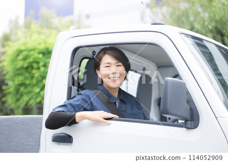 A middle-aged woman in work clothes driving a truck, easy to use for job changes and job offers, looking at the camera 114052909