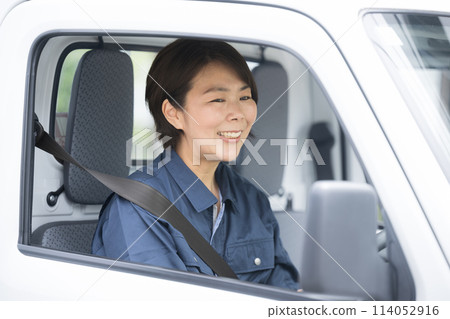 一名穿著工作服的中年婦女駕駛著卡車,透過後視鏡檢查後方、運輸和快遞行業的形像等。 一名穿著工作服的中年婦女駕駛著卡車,透過後視鏡檢查後方、運輸和快遞行業的形像等。 114052916