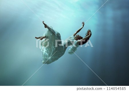 Angelic young girl in tender dress immersed in a world of tranquility and freedom. Girl levitating underwater with calmness Angelic young girl in tender dress immersed in a world of tranquility and freedom. Girl levitating underwater with calmness 114054585