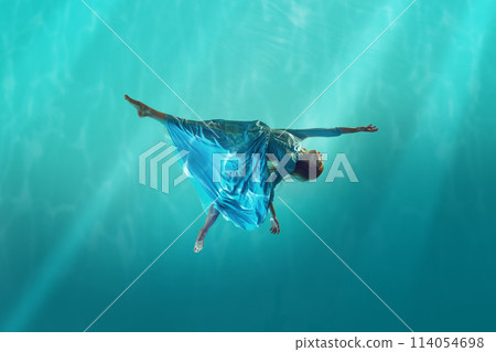 Lost in the current. Young redhead woman in elegant, tender white dress drowning into cyan water, deep ocean with sunlight Lost in the current. Young redhead woman in elegant, tender white dress drowning into cyan water, deep ocean with sunlight 114054698