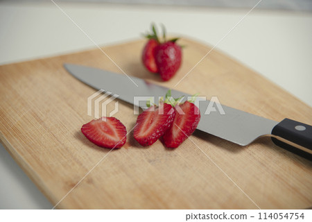 The strawberries are cut into slices. they lie on a wooden board and next to the knife The strawberries are cut into slices. they lie on a wooden board and next to the knife 114054754