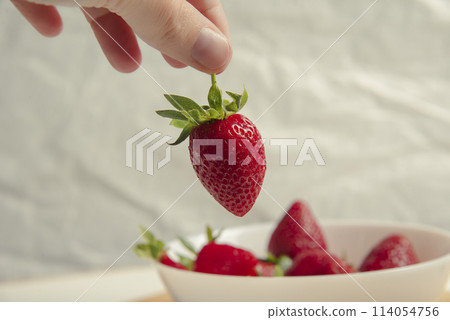 Close-up of strawberries in a woman hands against the background of strawberries in a bowl Close-up of strawberries in a woman hands against the background of strawberries in a bowl 114054756