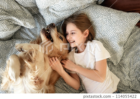 Cute Little Girl Playing With Golden Retriever Dog In Bed 114055422