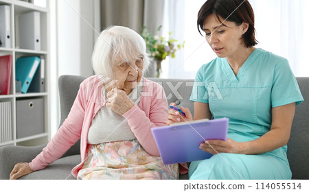 Doctor Reads Elderly Woman Health Documents In Bright Hallway 114055514