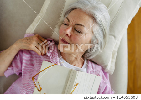 Top view of beautiful mature woman asleep with book. Weekend activity for older woman, relaxing at home. 114055608