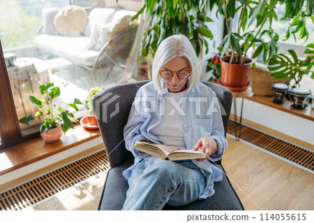 Beautiful mature woman reading book, feeling cozy and happy. Weekend activity for older woman, relaxing at home. Beautiful mature woman reading book, feeling cozy and happy. Weekend activity for older woman, relaxing at home. 114055615