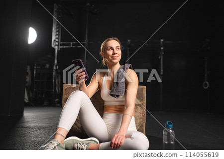 Fit woman resting after training in gym, scrolling on smartphone, checking workout app. Routine workout for physical and mental health. Fit woman resting after training in gym, scrolling on smartphone, checking workout app. Routine workout for physical and mental health. 114055619