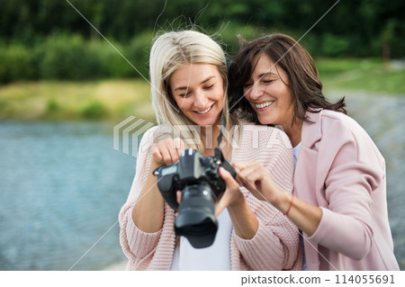 Adult daughter teaching mother how to take photos with professional camera, explaining technology, laughing. Mother's Day concept. 114055691