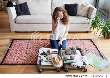 Beautiful woman planning summer vacation abroad, sitting on floor, packing suitcase. Solo traveler making phone call. Beautiful woman planning summer vacation abroad, sitting on floor, packing suitcase. Solo traveler making phone call. 114055791
