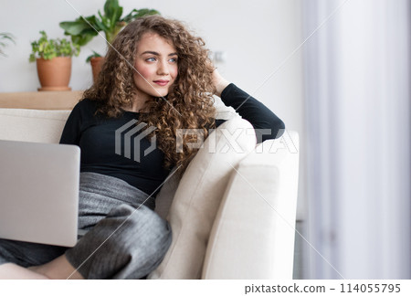 Beautiful woman planning summer vacation abroad, going on trip alone. Sitting on sofa working on itinerary on laptop. 114055795