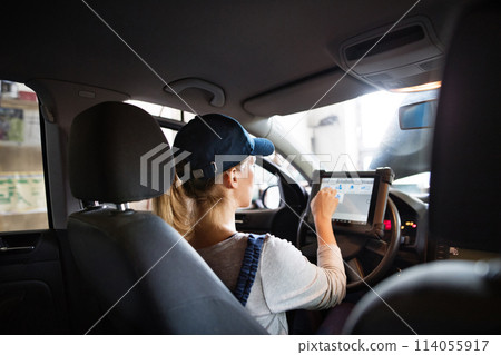 Female auto mechanic using diagnostic tool, scanner, running diagnostic on car. Beautiful woman sitting inside of car, performing diagnostic test. Female auto mechanic using diagnostic tool, scanner, running diagnostic on car. Beautiful woman sitting inside of car, performing diagnostic test. 114055917