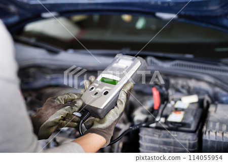 Female auto mechanic using diagnostic tool, scanner, running diagnostic on car. Beautiful woman working in a garage, wearing blue coveralls. Female auto mechanic using diagnostic tool, scanner, running diagnostic on car. Beautiful woman working in a garage, wearing blue coveralls. 114055954