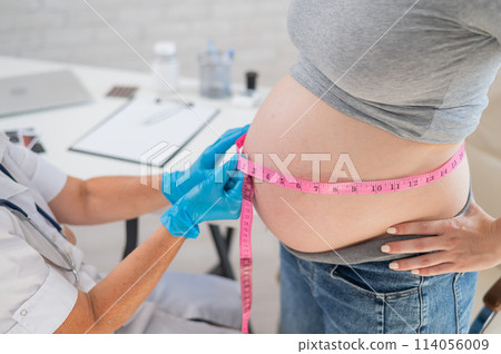 Doctor measuring the volume of a pregnant woman's abdomen using a tape in inches. Doctor measuring the volume of a pregnant woman's abdomen using a tape in inches. 114056009