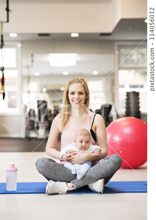 Portrait of new mom on group exercise class in gym. Moms staying active while boding with babies. 114056012