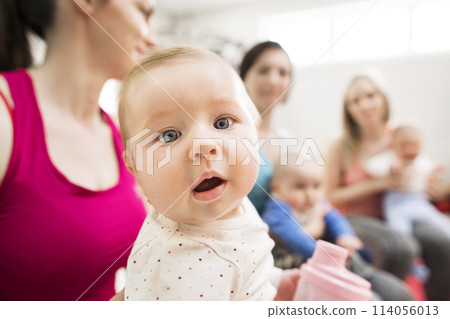 Baby movement class. Parents helping babies to improve motor skills, proper movement on fitball. Pediatric physical therapist leading class. Mothers exercising with babies. 114056013