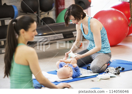 Mother changing diaper during group exercise class. Moms staying active, working out with baby in gym, bonding. Mother changing diaper during group exercise class. Moms staying active, working out with baby in gym, bonding. 114056046